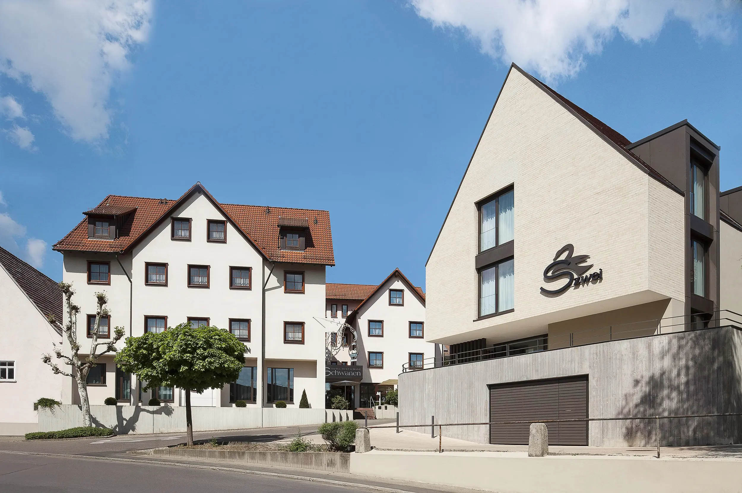Weiße Gebäude im traditionellen Stil mit roten Dächern unter blauem Himmel, Baum im Vordergrund.