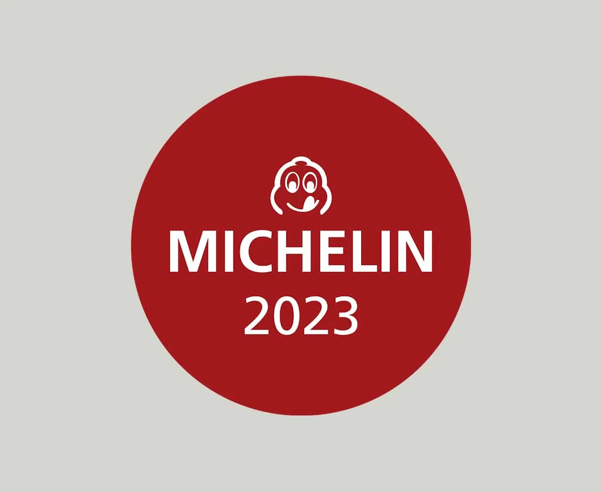 Roter Kreis mit dem Michelin-Logo und der Aufschrift „MICHELIN 2023“ auf grauem Hintergrund.