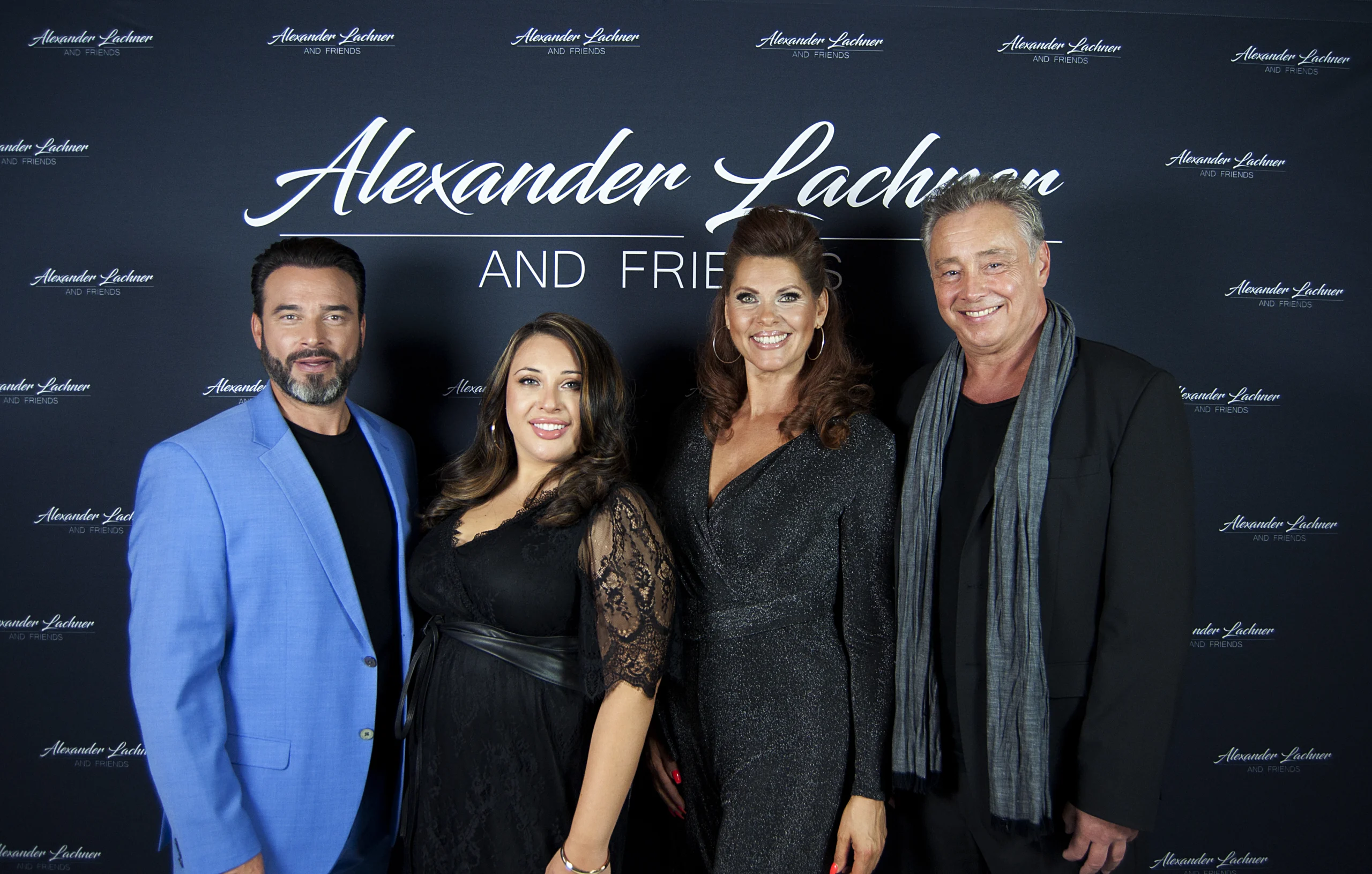 Vier Personen posieren lächelnd bei einem Event vor einer Wand mit Alexander Lachner and Friends-Schriftzug.