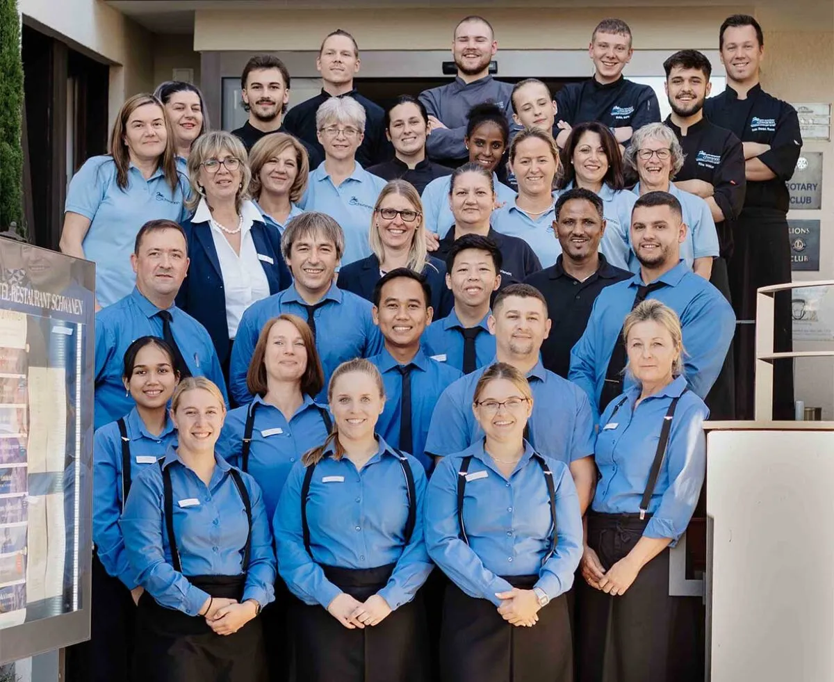 Eine Gruppe von Restaurantmitarbeitern in blauer Uniform posiert lächelnd auf einer Treppe für ein Gruppenfoto.