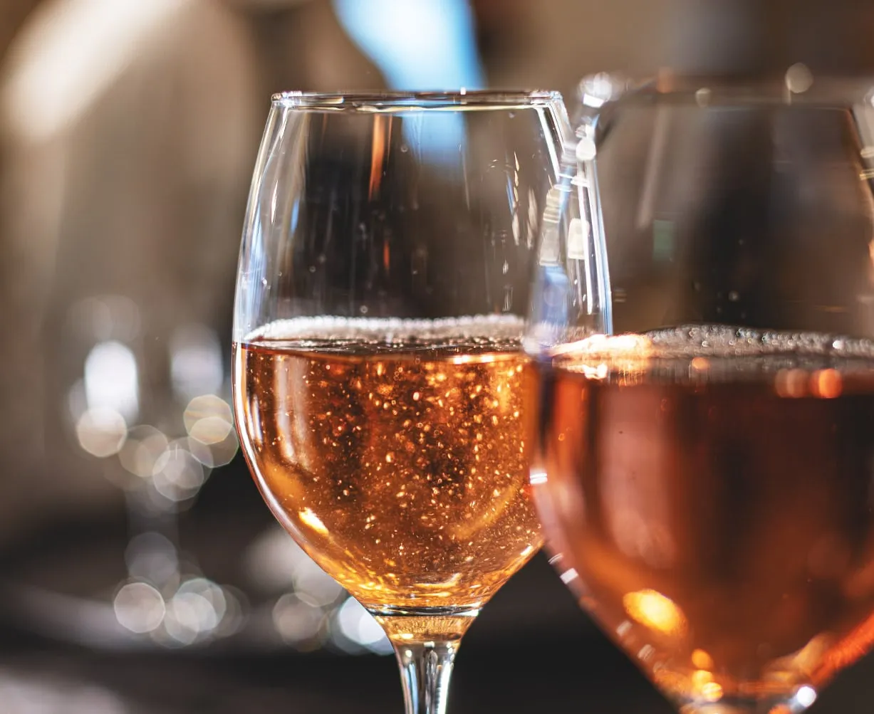 Zwei Gläser Roséwein mit Schaum und Bläschen, im Hintergrund unscharf weitere Gläser.