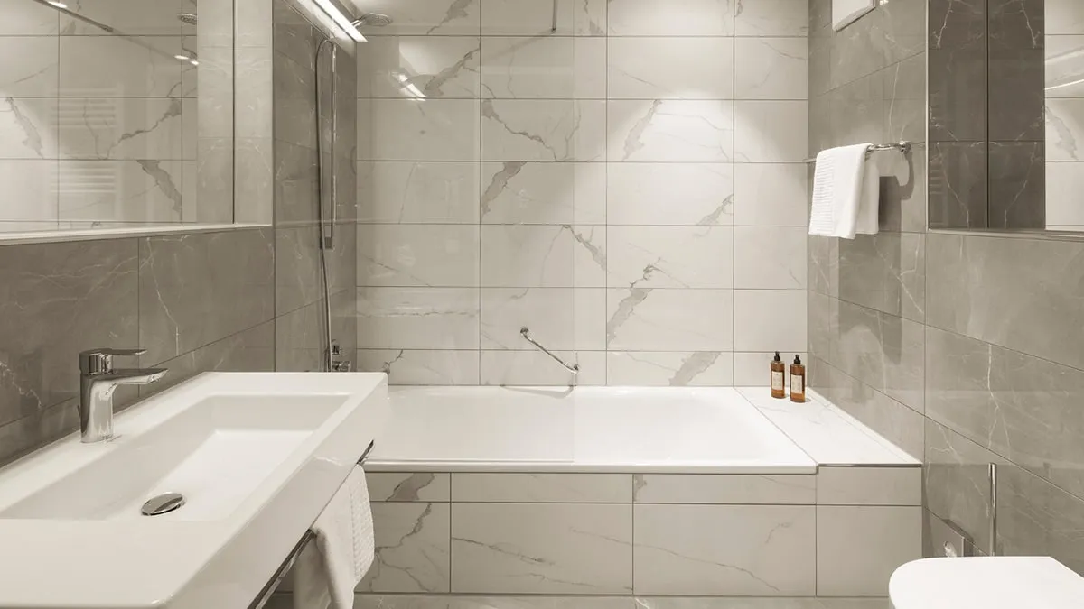 Badezimmer-Deluxe Modernes Badezimmer mit Marmorfliesen, Badewanne, Waschbecken, Handtuchhalter, Spiegel und zwei Flüssigseifenspendern.