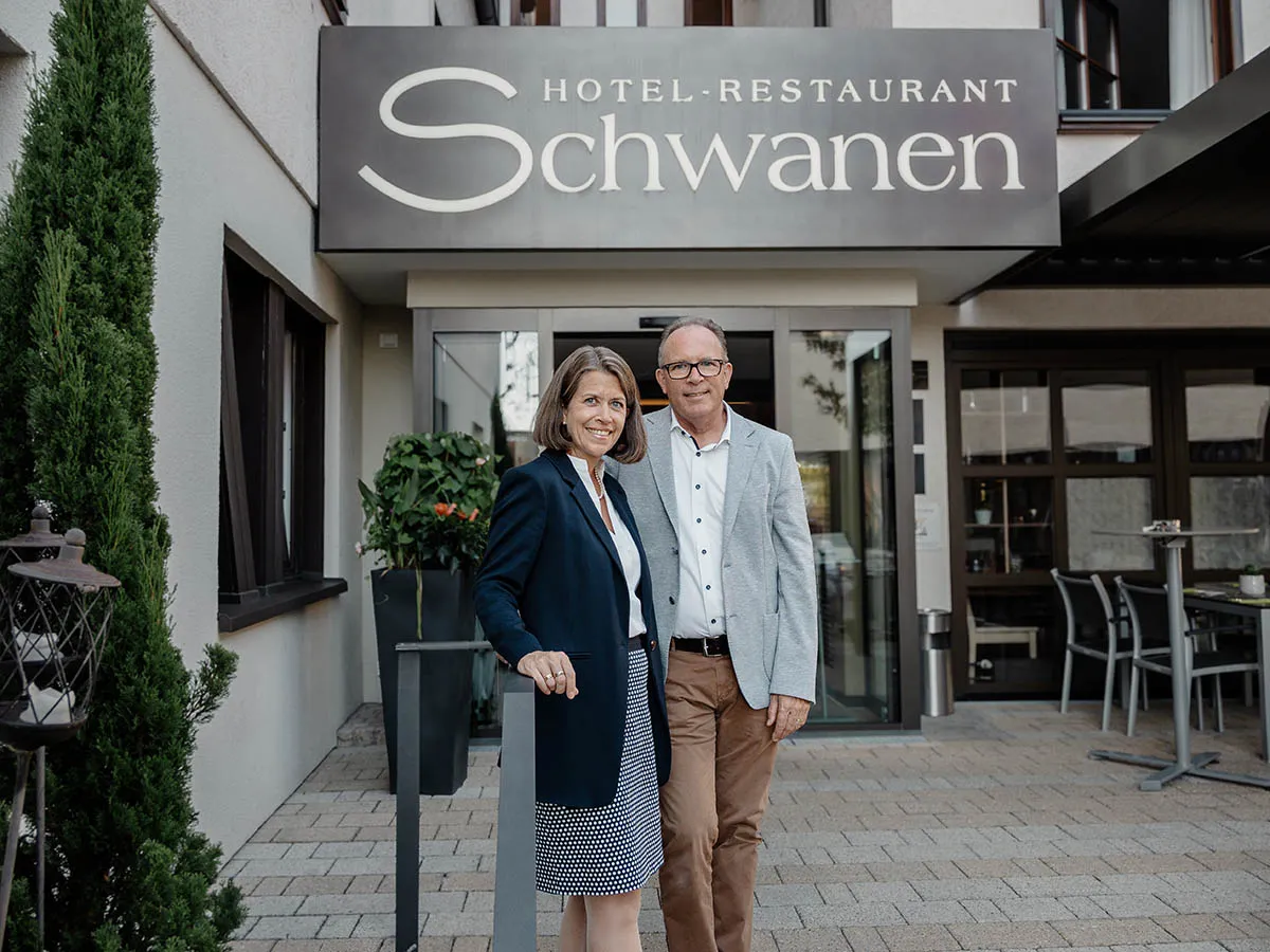 Zwei Personen stehen vor dem Eingang des Hotel-Restaurants Schwanen, lächeln in die Kamera.