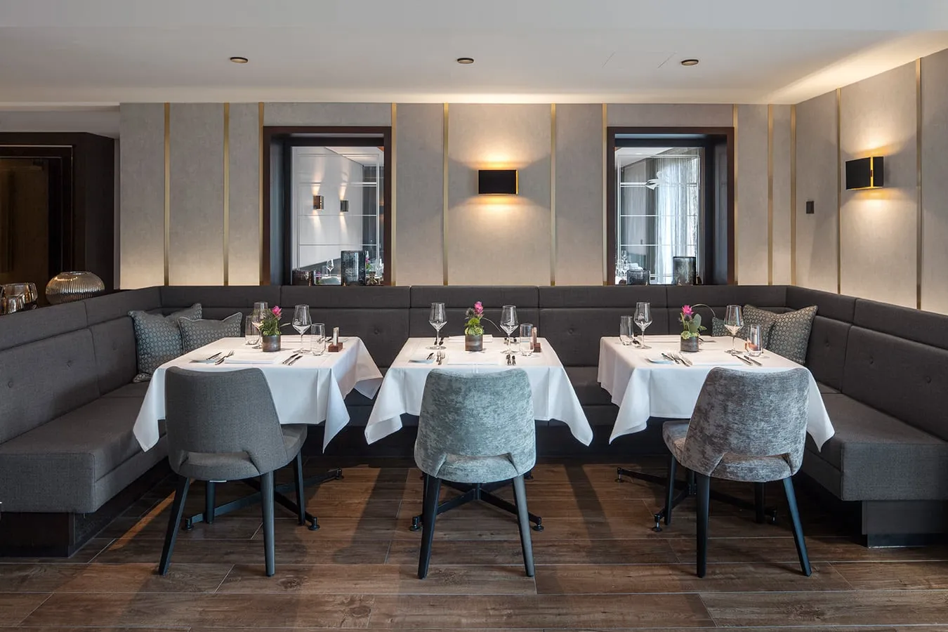 Elegantes Restaurant mit drei gedeckten Tischen, grauen Stühlen und indirekter Beleuchtung, klassische Atmosphäre.