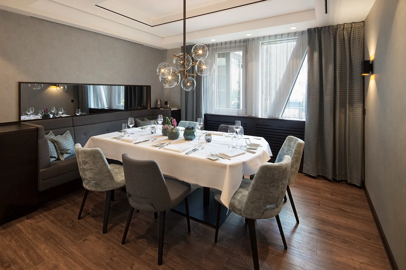Elegantes Esszimmer mit gedecktem Tisch für acht Personen, moderne Leuchte, Fenster mit Vorhängen, Holzboden.