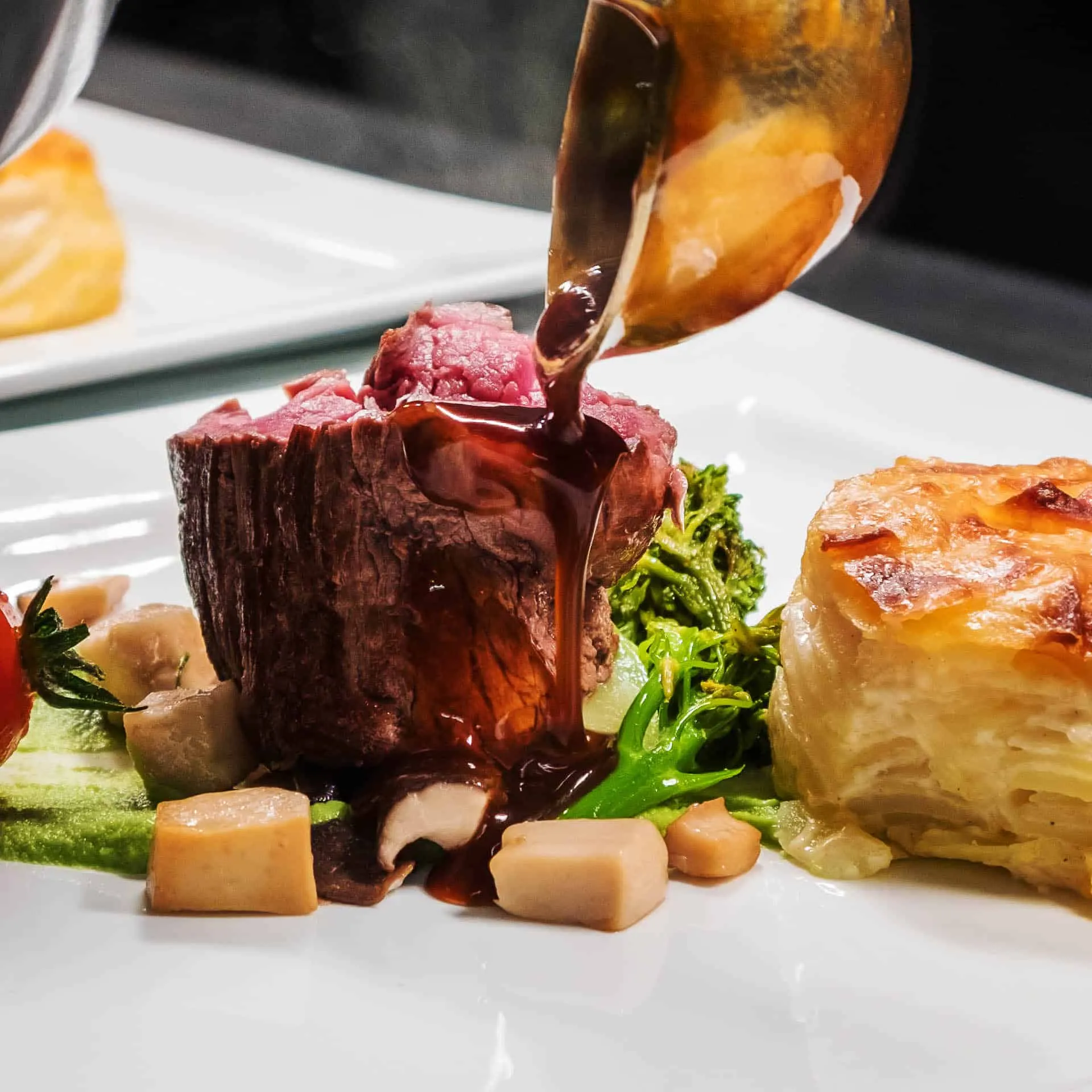 Ein saftiges Rinderfilet wird mit roter Soße übergossen, begleitet von Brokkoli, Würfeln und Kartoffelgratin auf einem Teller.