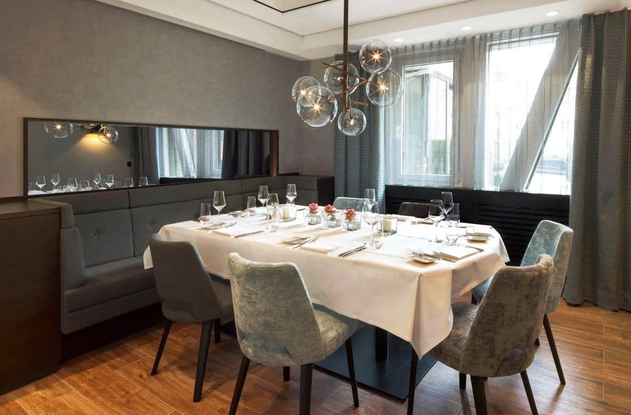 Elegantes Esszimmer mit gedecktem Tisch für sechs Personen, modernen grauen Stühlen und großer Fensterfront.