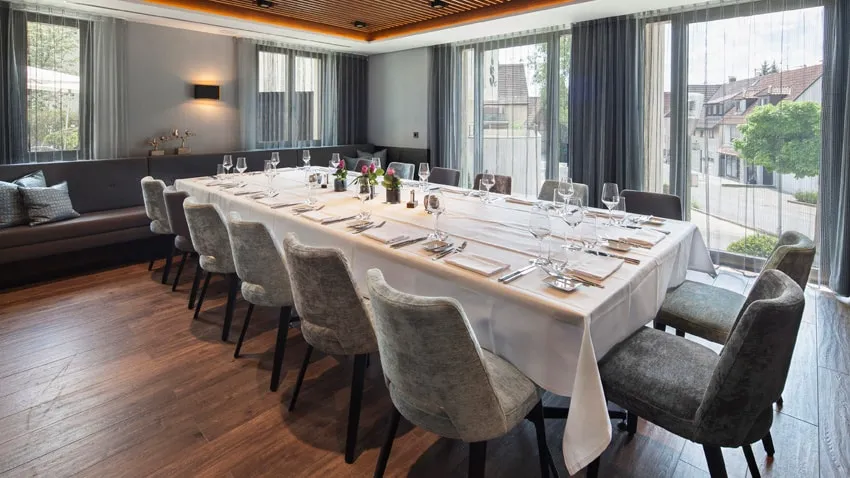 Eleganter Konferenzraum mit großem Tisch, gedeckt für zwölf Personen, Holzfußboden und großen Fenstern mit Blick nach draußen.