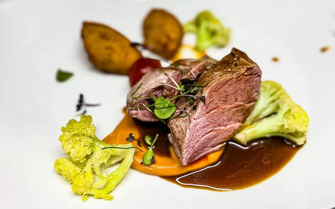 Roastbeef auf Soße mit Blumenkohl, Kartoffeln und Kräutern auf Teller angerichtet.