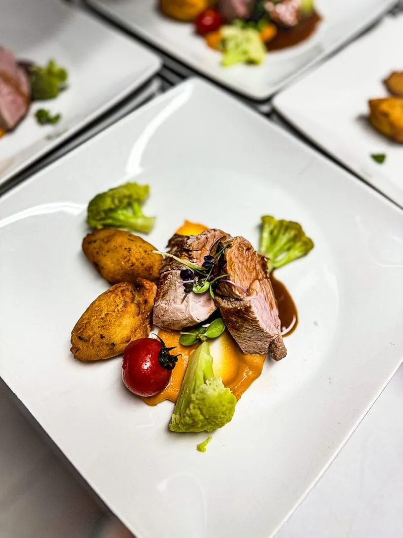 Gourmetgericht mit gebratenem Fleisch, Kartoffeln, Brokkoli, Tomate und Soße auf einem weißen Teller angerichtet.