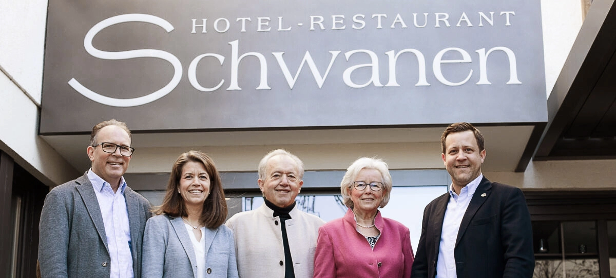 Fünf Personen stehen lächelnd vor dem Eingang des „Hotel-Restaurant Schwanen“, das Schild ist im Hintergrund sichtbar.