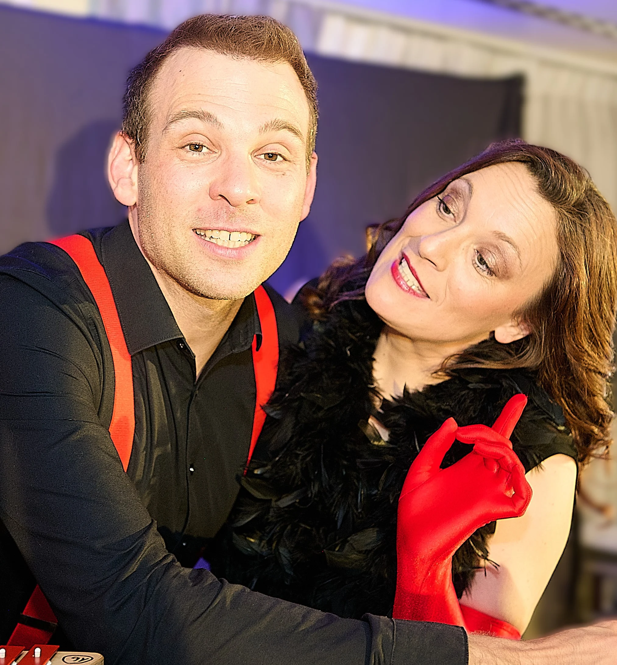 Ein Mann in schwarzem Hemd mit roten Hosenträgern und eine lächelnde Frau mit schwarzem Schal.