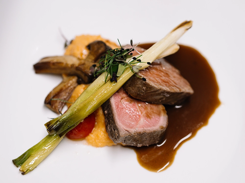 Schwanen_Food_KG Gericht mit zwei Scheiben Rindfleisch, Gemüsebeilage aus Pilzen und Lauch, serviert mit einer dunklen Sauce und Püree.