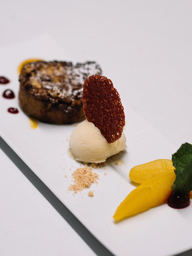 Schwanen_Nachtisch Dessertteller mit Schokoladenkuchen, Vanilleeis, karamellisiertem Keks, Mangostreifen und Fruchtsoße.